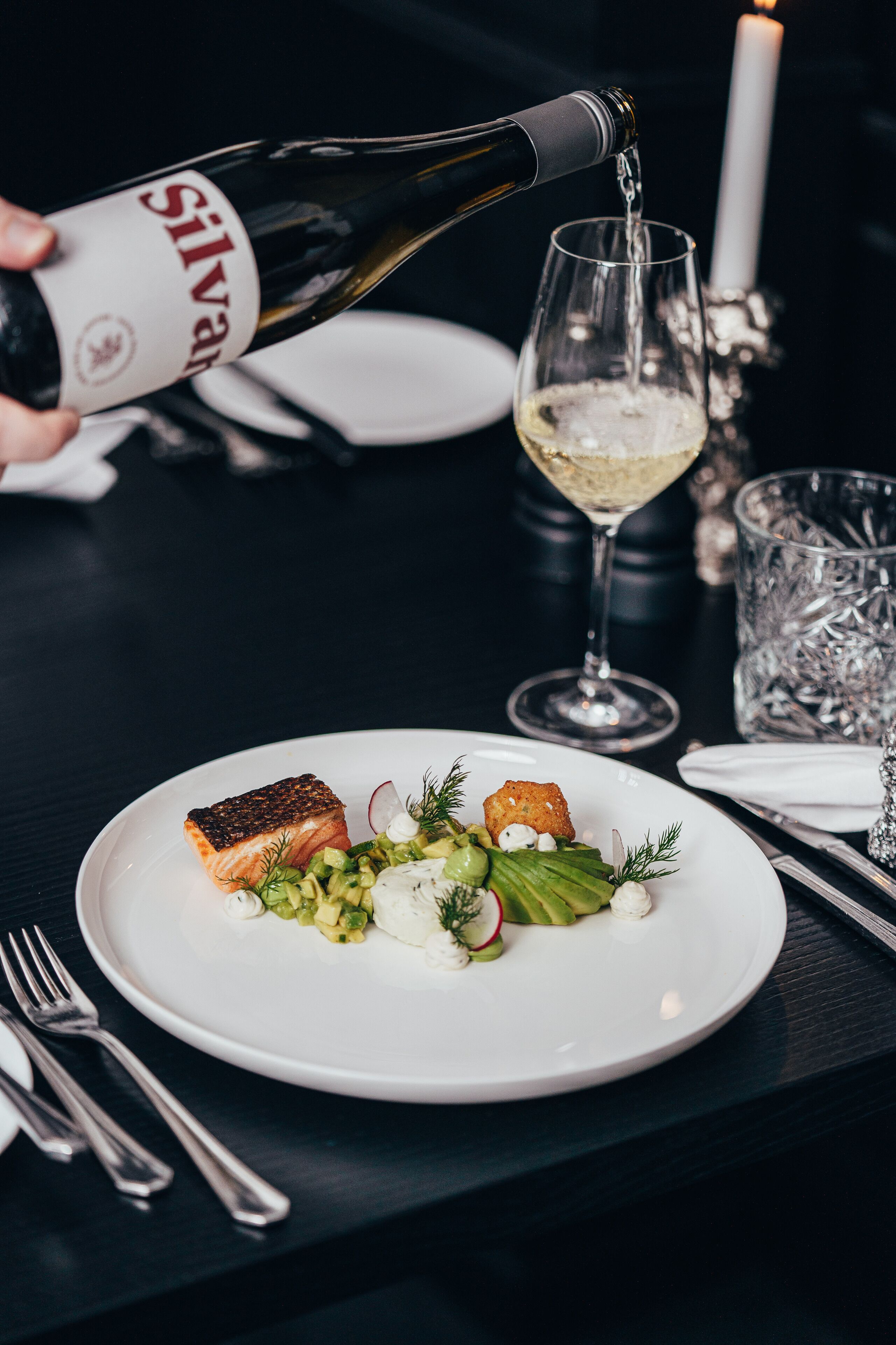 Una mesa de comedor con un plato de comida, una botella de vino y una copa de vino blanco.