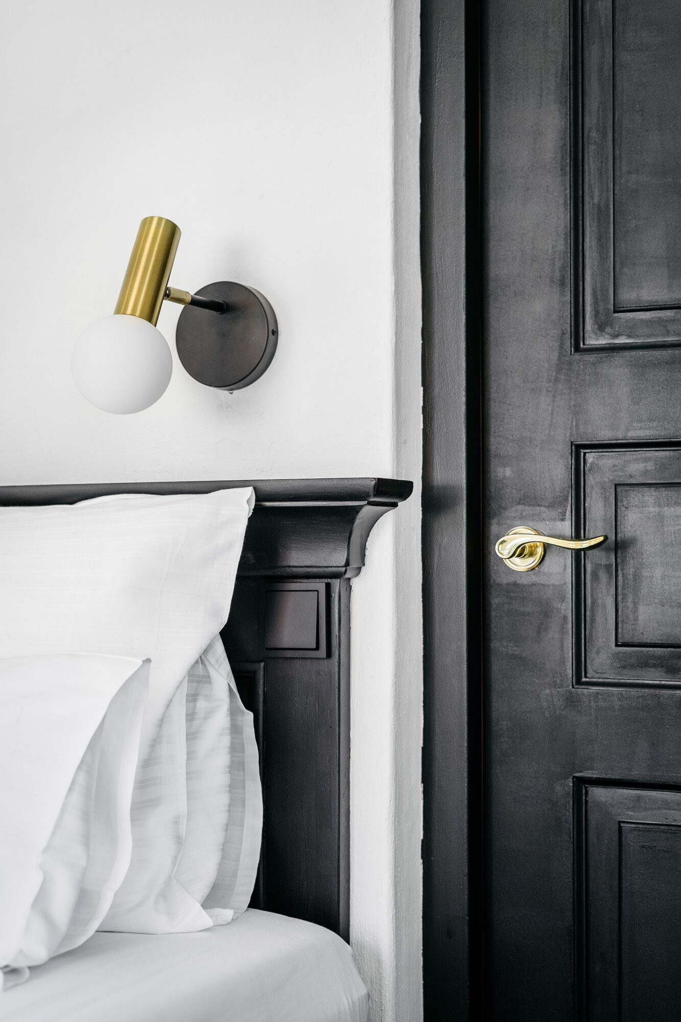 Une porte en bois sombre avec une poignée en laiton, un mur blanc et un lit recouvert de draps blancs.