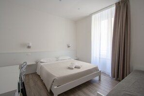 Une chambre à coucher propre et moderne, avec un lit simple, une table de chevet et une grande fenêtre avec des rideaux.