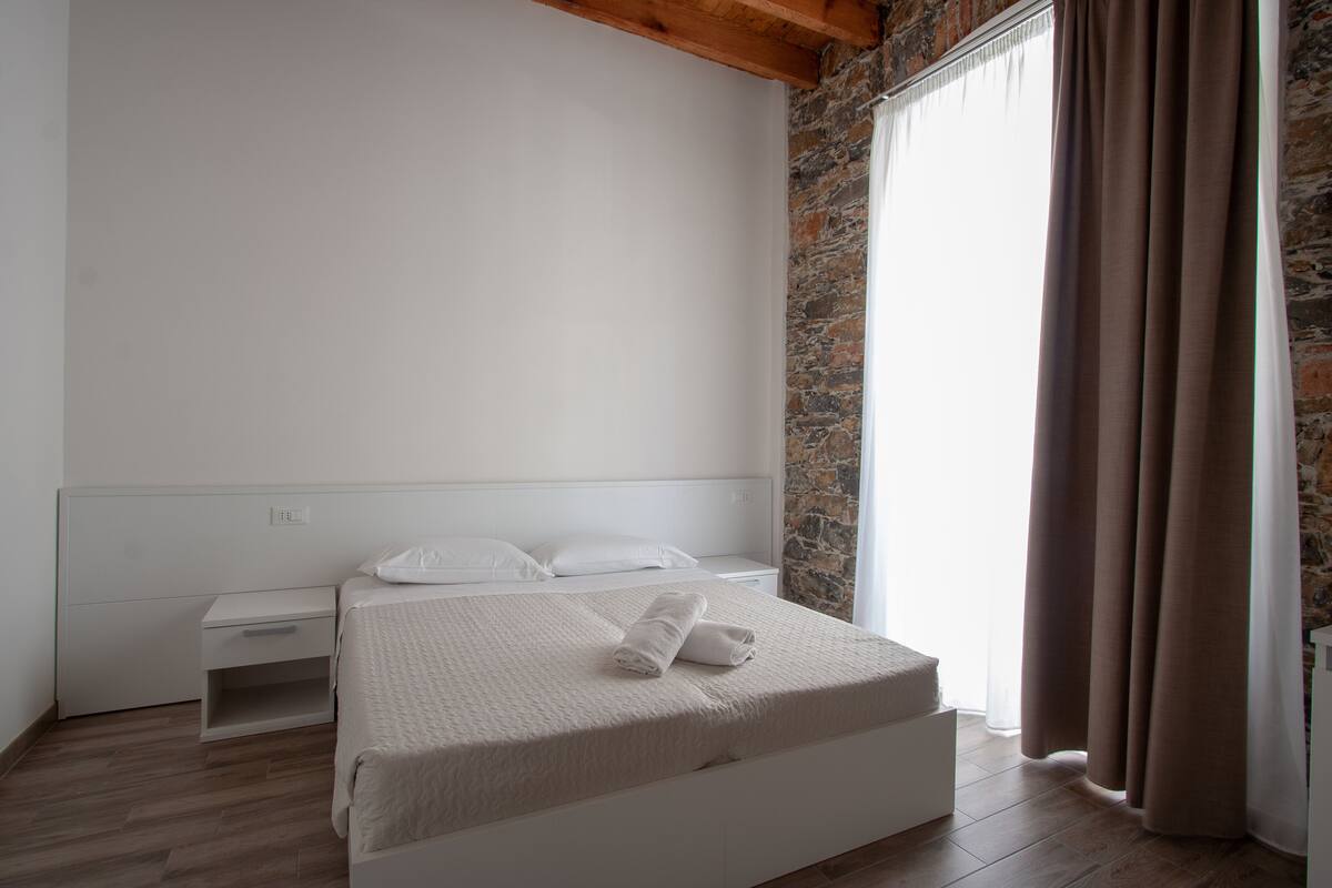 Ein schlichter Schlafzimmerraum mit einem Bett, einem Nachttisch und einer Wand mit Steinoptik.