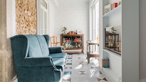 A living room with a blue sofa, a wooden cabinet with glass doors, and a patterned floor. - 1898 Home & Suites (Lisbon)