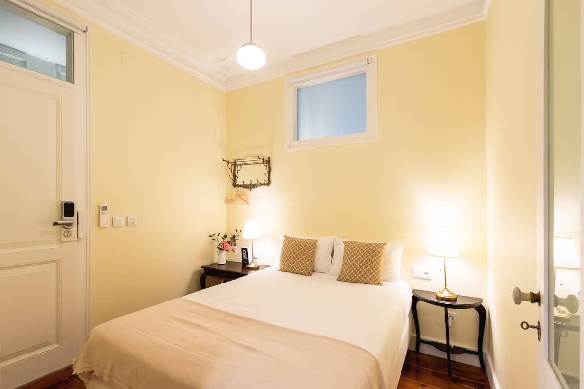 A hotel room with a bed, bedside tables, a window, and a door.