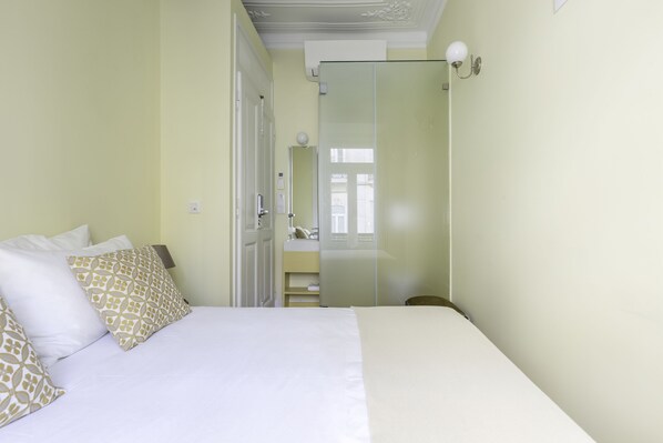 A hotel room with a bed, a nightstand, a mirror, and a door leading to a bathroom.