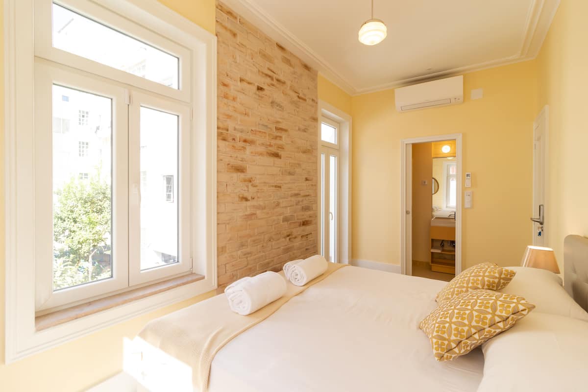 A bedroom with a large bed, a brick accent wall, and a view through a window.
