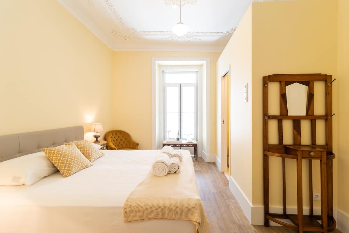 A hotel room with a large bed, a wooden side table, a chair, and a wooden shelf.