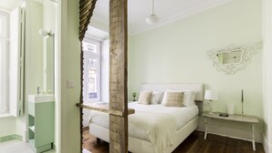 A bedroom with a bed, bedside table, and a mirror on the wall. - 1898 Home & Suites (Lisbon)