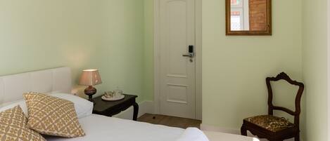 A neatly made bed with rolled towels, a bedside lamp, a chair, and a door in a room with light green walls and a white ceiling.