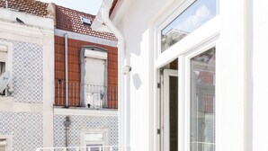 A balcony with a wooden table and chairs, a glass door leading to a patio area, and a tiled wall with a patterned design. - 1898 Home & Suites (Lisbon)