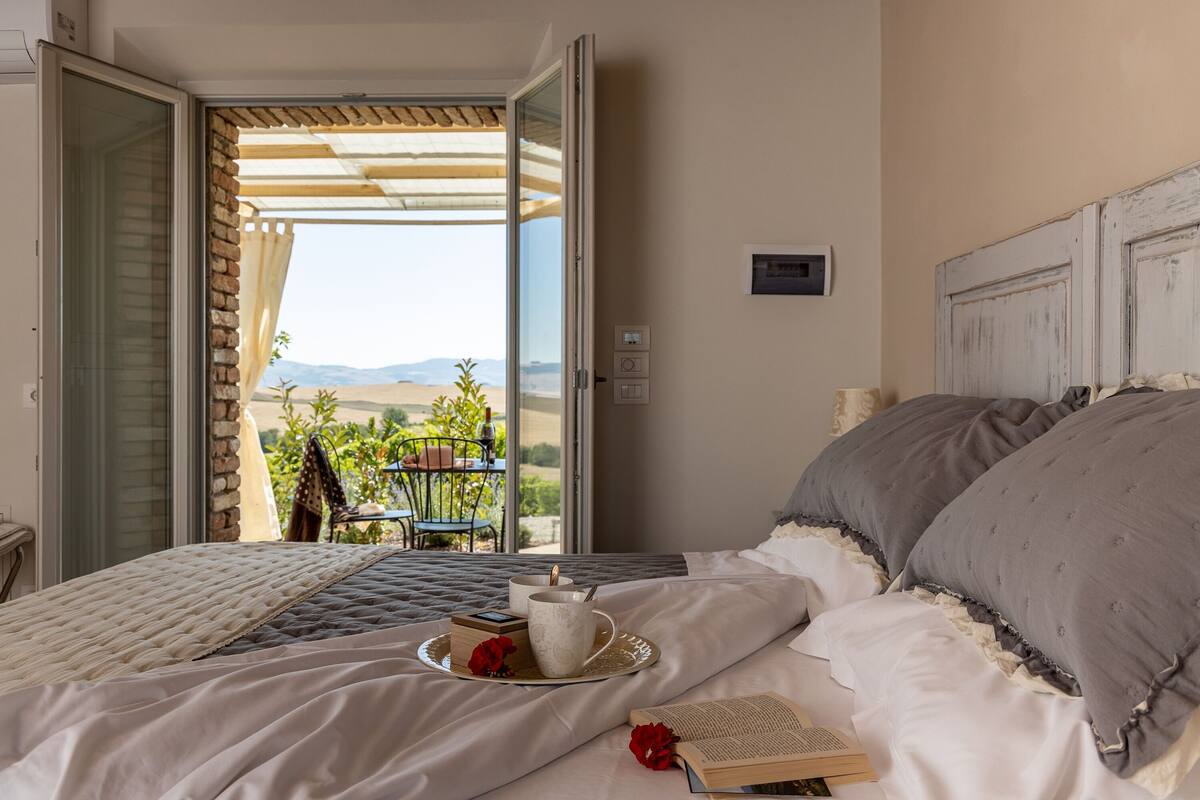 A bedroom with a bed, a tray with a cup and a book, and a view of the outdoors.