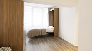 A bedroom with a bed, wooden wardrobe, and a window with curtains.
