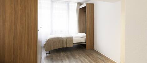 A bedroom with a bed, wooden wardrobe, and a window with curtains.