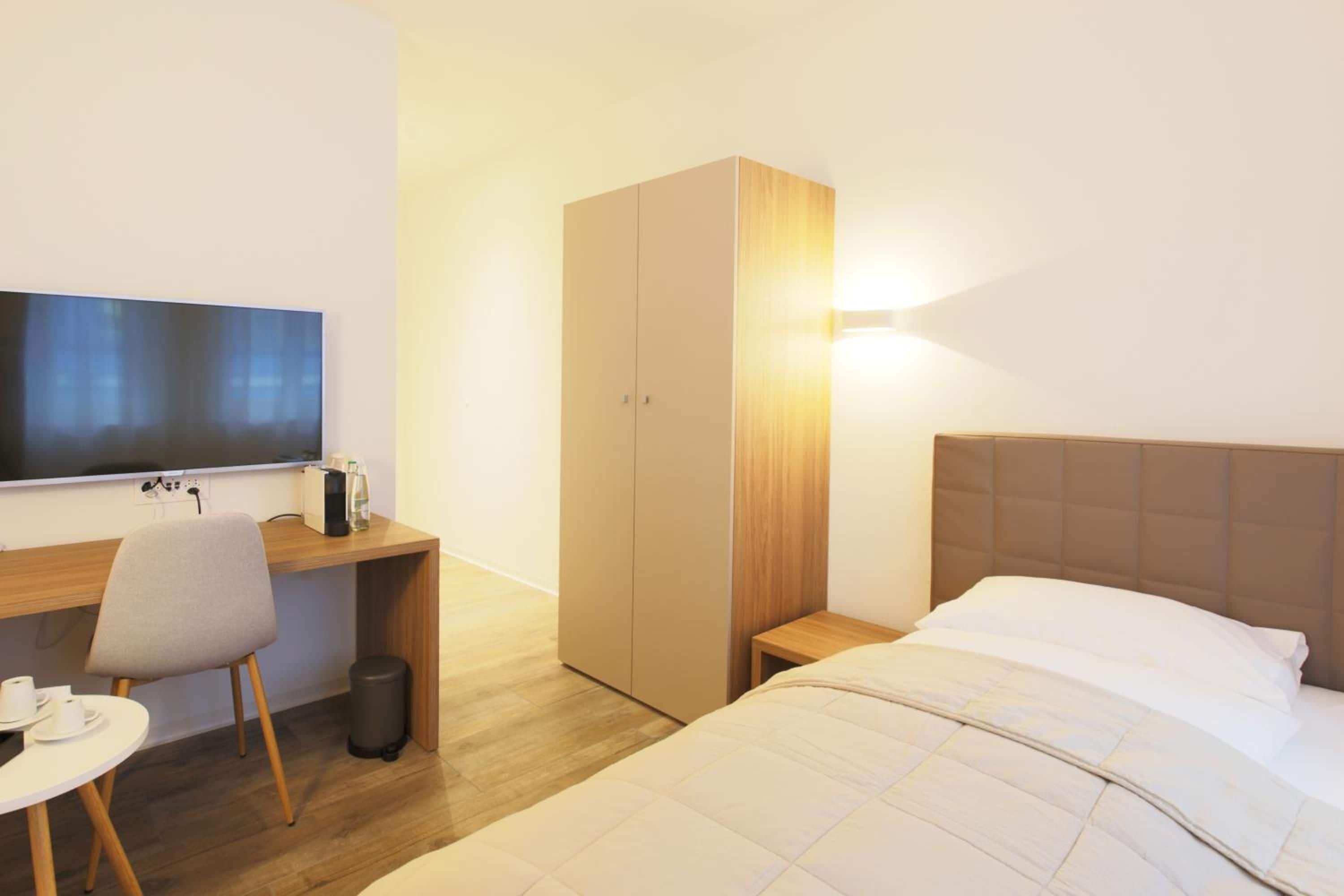 Een hotelkamer met een bed, een bureau met stoel, een kledingkast en een televisie.
