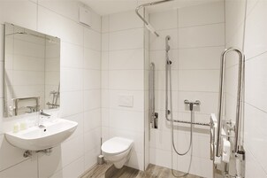 Un baño moderno con lavamanos, inodoro y cabina de ducha a ras de suelo con barras de apoyo.