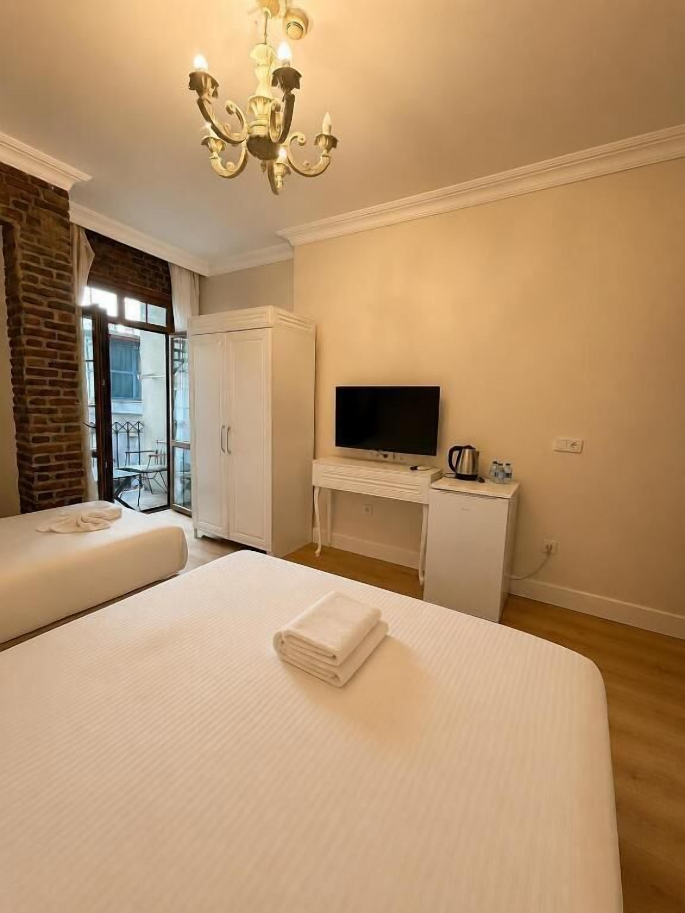 A hotel room with a large bed, a desk with a flat-screen TV, a white wardrobe, and a brick wall.