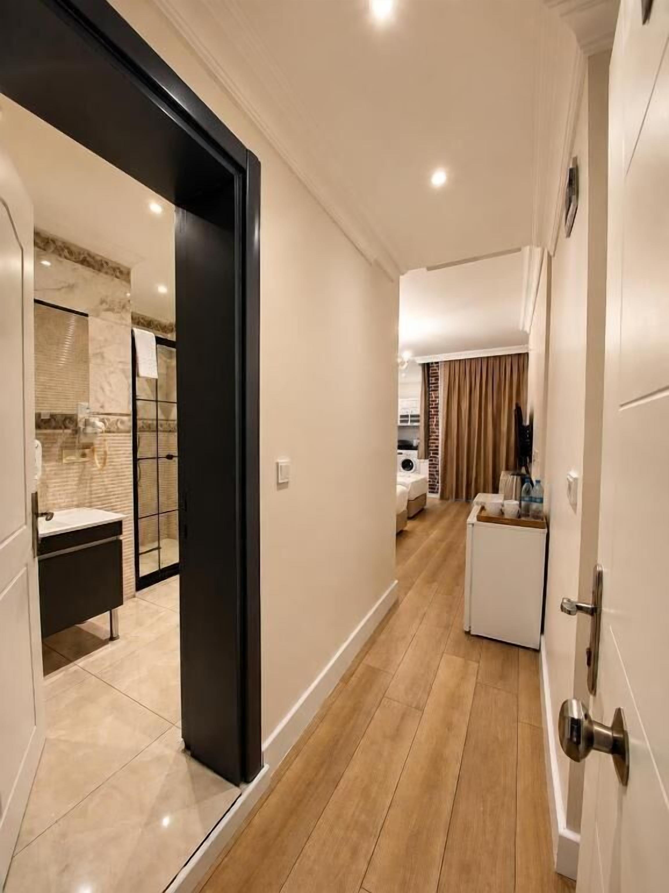 A hallway with a modern kitchen area, a small seating area, and a door leading to a bathroom.
