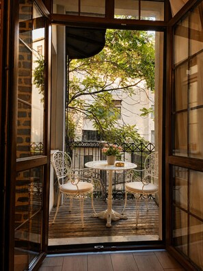 An open balcony with a round table and two chairs, a potted plant, and a view of the surrounding buildings.