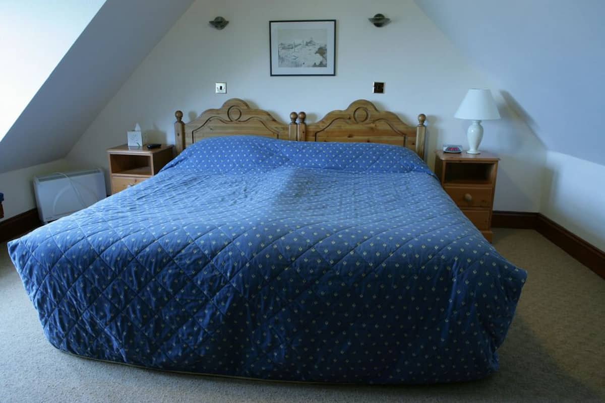 Ein Schlafzimmer mit einem großen Bett, zwei Nachttischen, einer Wandlampe und einem gerahmten Bild an der Wand.