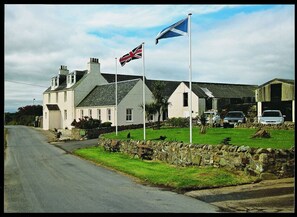 A two-story house with a stone wall and a grassy lawn. - Gigha Hotel (Isle of Gigha)