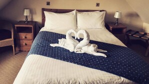 A hotel room with a large bed, two nightstands, a lamp on each nightstand, a picture on the wall, and a towel sculpture on the bed. - Gigha Hotel (Isle of Gigha)