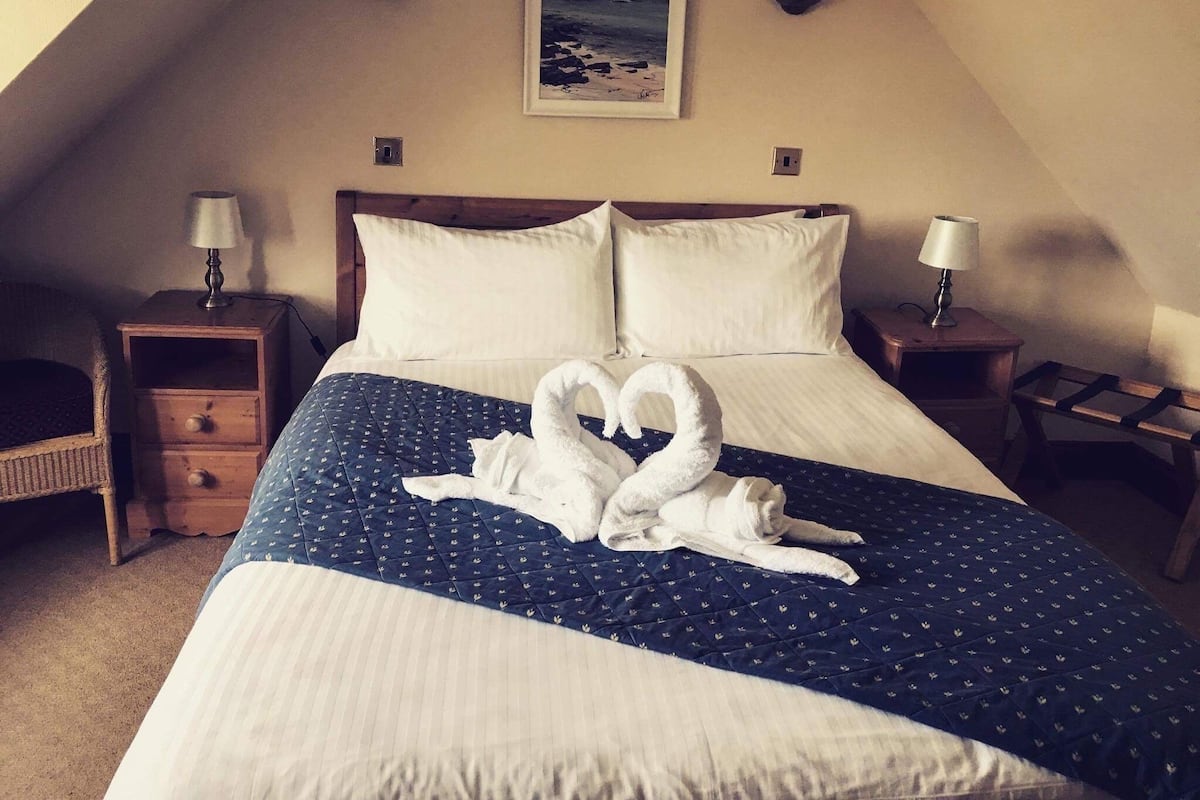 Ein Hotelzimmer mit einem großen Bett, zwei Nachttischen, einer Lampe auf jedem Nachttisch, einem Bild an der Wand und einer Handtuchskulptur auf dem Bett.