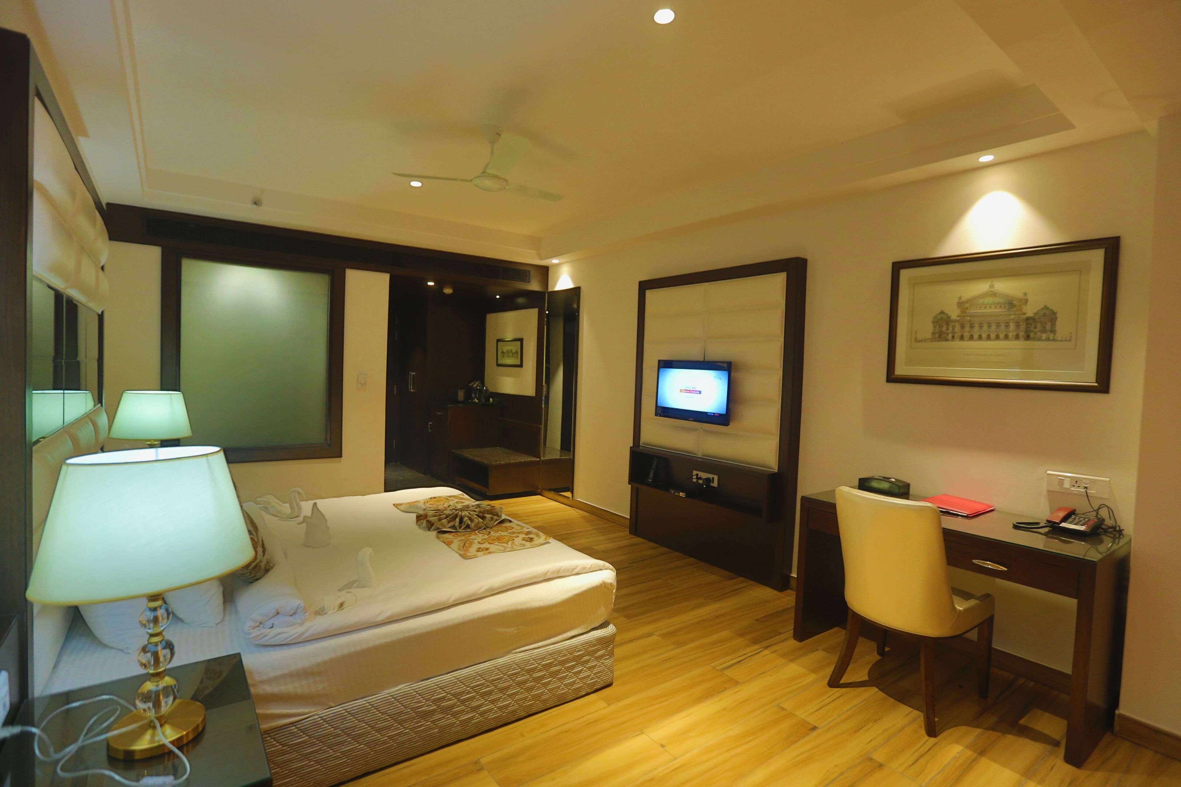 Habitación de hotel con cama, escritorio, silla, televisor y un cuadro en la pared.