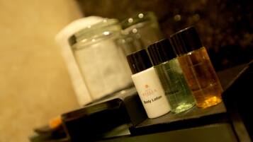 Una encimera de baño con artículos de aseo, incluyendo una botella etiquetada “Hotel Stella Continental Body Lotion”, un envase de champú y un tarro de crema hidratante.