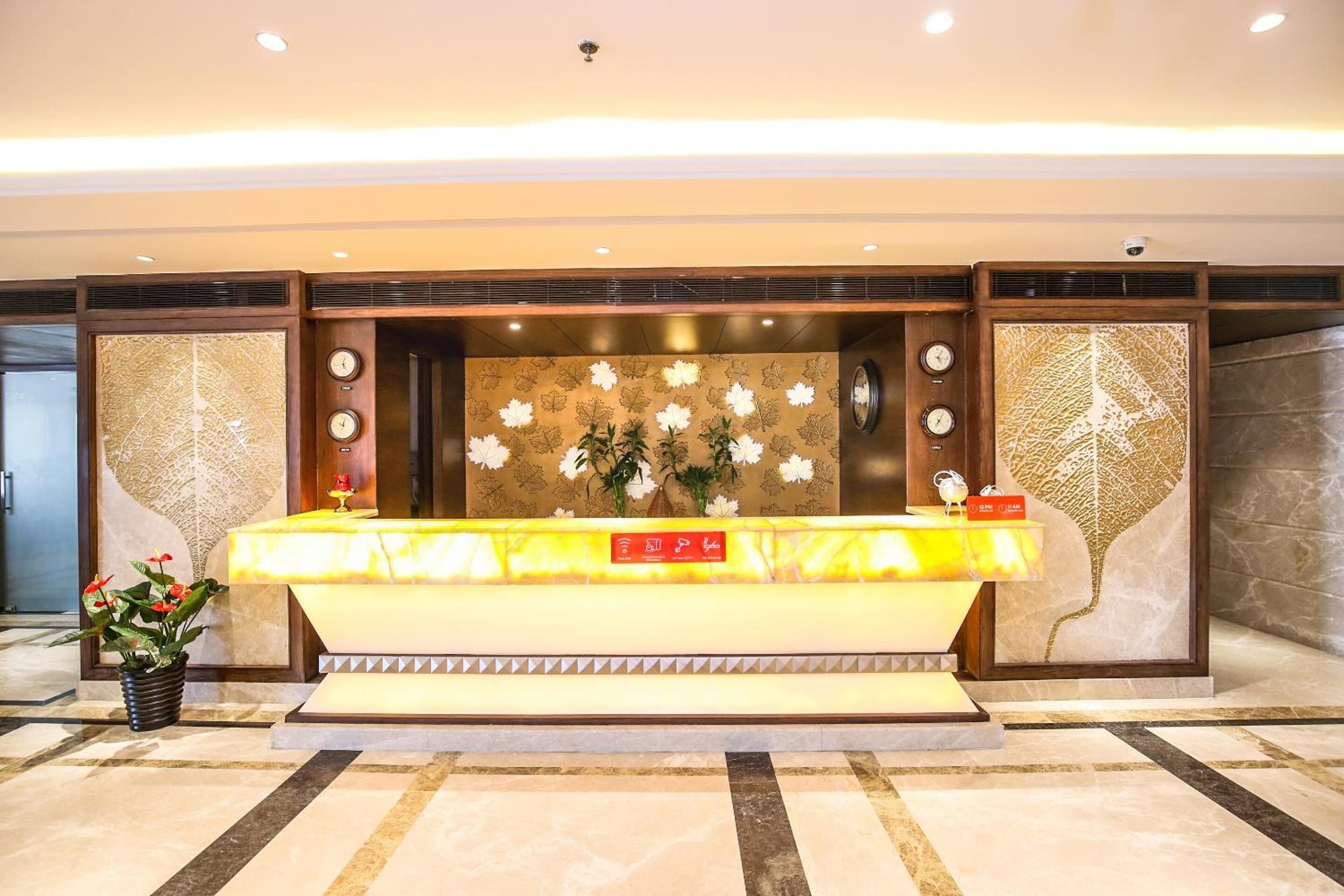 A reception desk with a marble counter, two clocks, and a floral wall decoration.