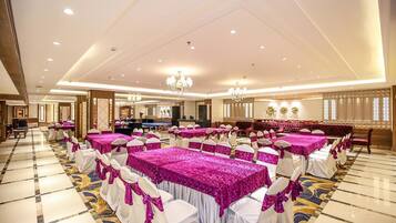 Une salle de banquet avec des rangées de tables recouvertes de nappes roses, des chaises blanches ornées de rubans roses et des lustres au plafond.
