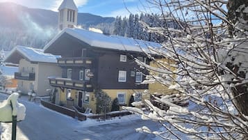 Un edificio cubierto de nieve con una torre destacada, rodeado de árboles cargados de nieve y un cielo despejado.