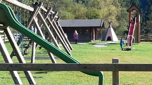 A playground with a slide, swings, and a small building in the background. - Pension Haus Rohrmoser (Annaberg-Lungoetz)