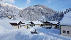 A snow-covered mountain village with chalet-style buildings, a clear sky, and a snow-covered road. - Pension Haus Rohrmoser (Annaberg-Lungoetz)
