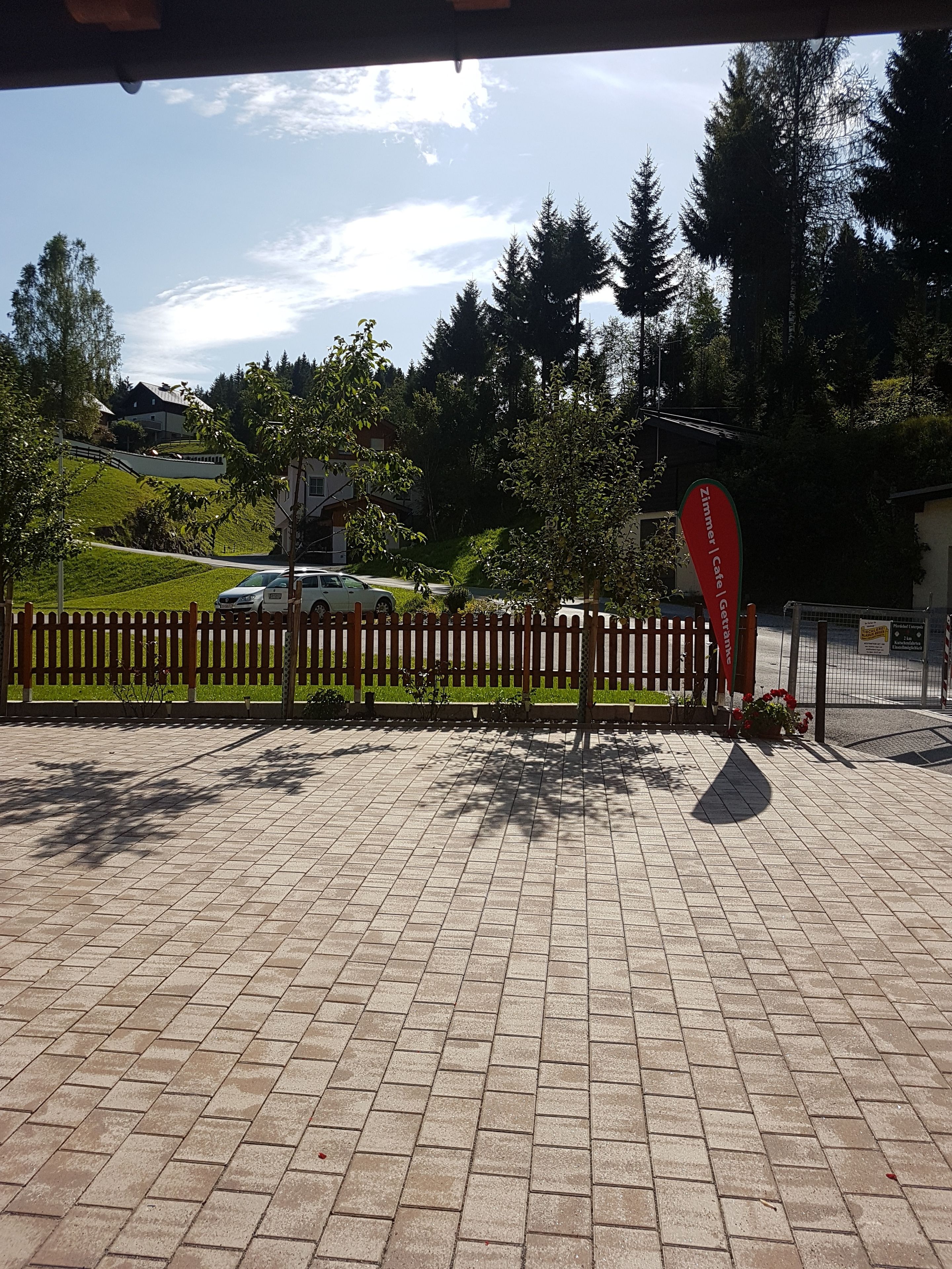 A paved outdoor area with a wooden fence, a sign for 'Zimmer Cafe', and a car parked nearby.