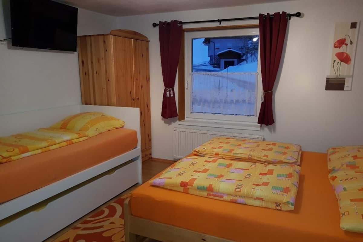 A bedroom with two single beds, a wooden wardrobe, a window with curtains, and a radiator.