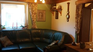 A cozy living room with a curved black leather sofa, a wooden coffee table, and a wooden ceiling with exposed beams. - Pension Haus Rohrmoser (Annaberg-Lungoetz)