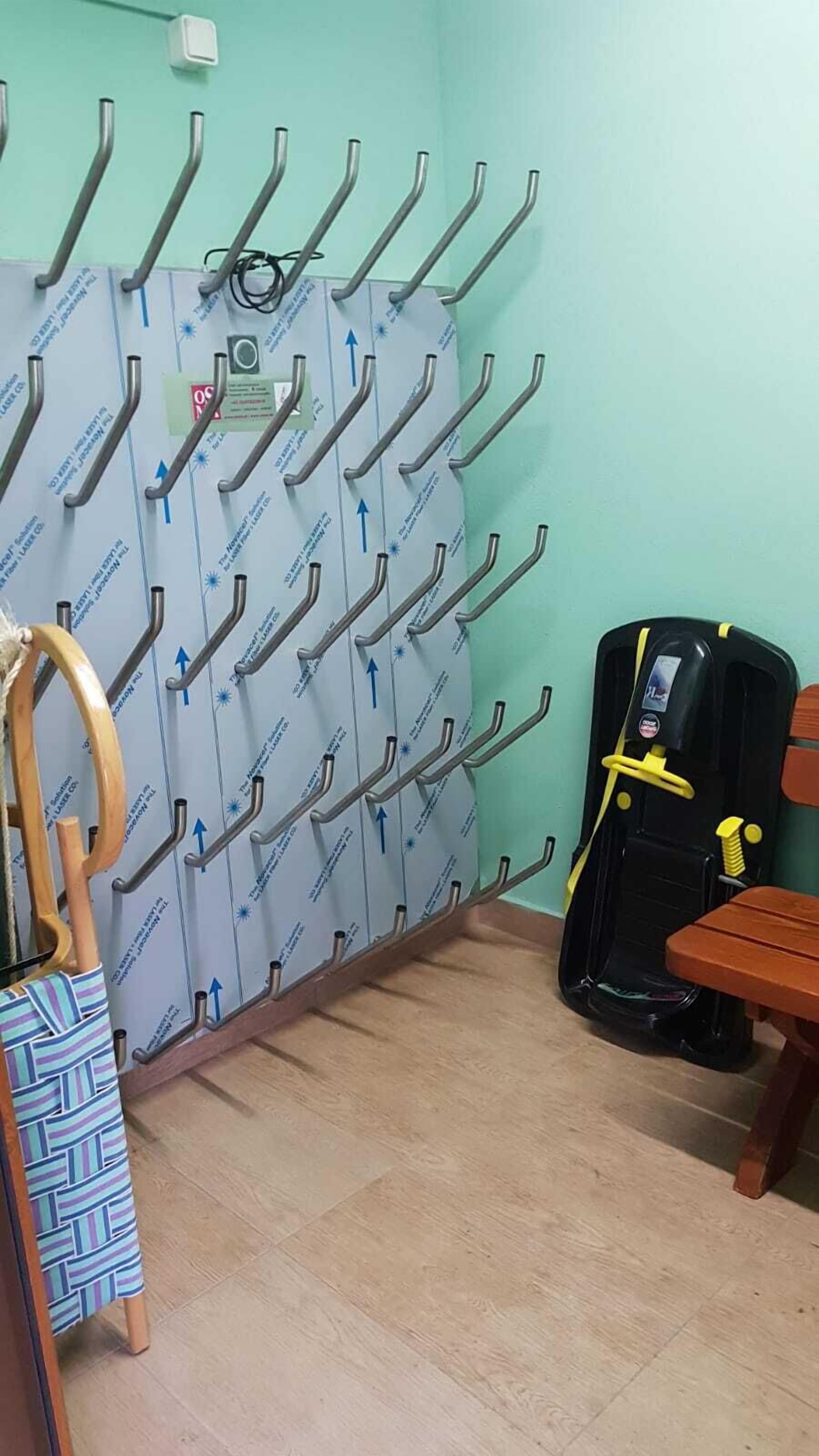 Una habitación con un perchero metálico de pared, un dispensador de agua negro, un banco de madera y una bolsa estampada colgada de un gancho.
