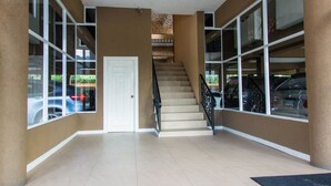 A spacious indoor area with a staircase leading to an upper level, large windows, and a clean, tiled floor. - Kings Manor 06 by Pro Homes Jamaica (Kingston)