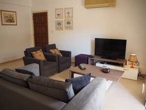 A living room with a sofa, two armchairs, a coffee table, a TV, and a lamp.