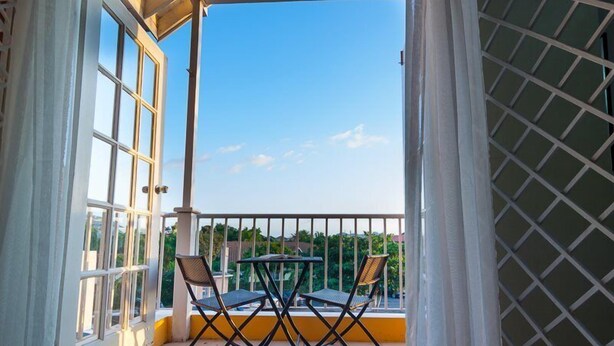 Ein Balkon mit Tisch und Stühlen, Blick zum Himmel und einem Gitterzaun.