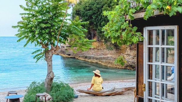 A person sitting on a log by a beach with a clear view of the sea and a building with a window. - Azureva - Roquebrune Cap Martin (Roquebrune-Cap-Martin)