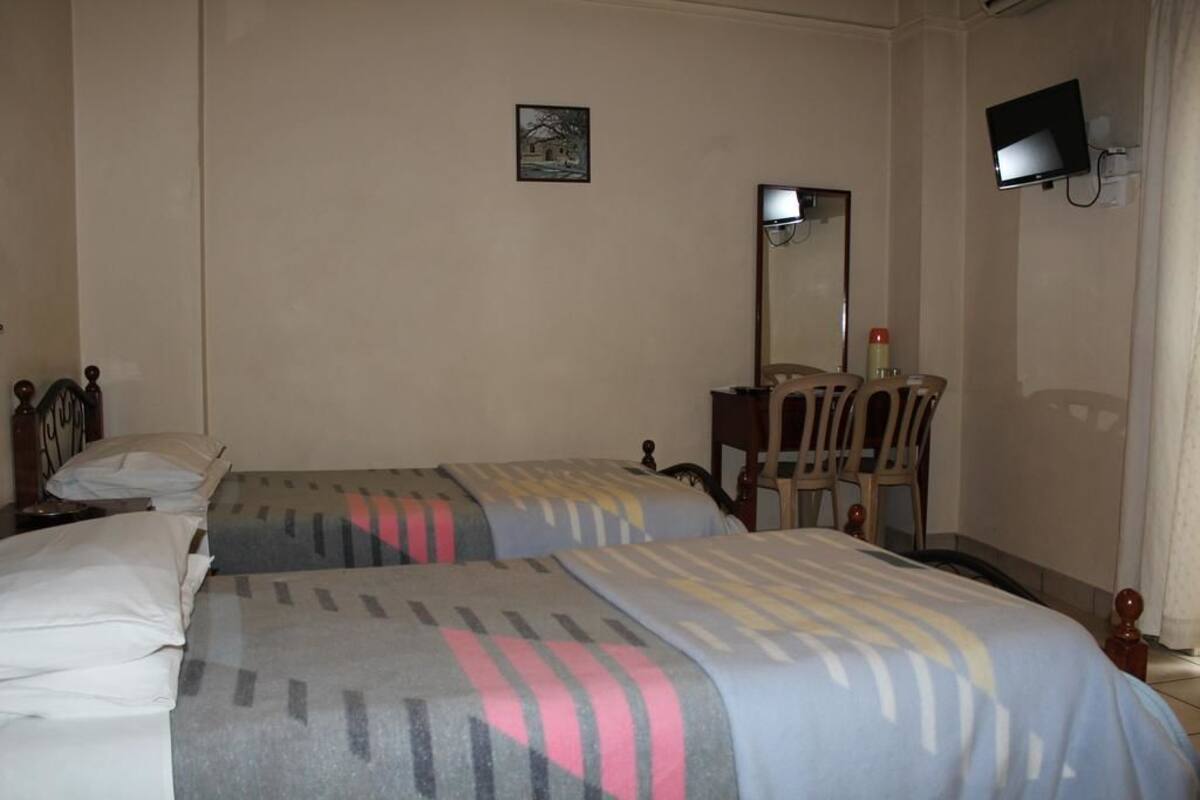 Une chambre d’hôtel avec deux lits simples, un bureau avec une chaise, une télévision et un petit tableau accroché au mur.