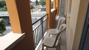 A balcony with two white plastic chairs and a view of a street with vehicles and pedestrians. - Delphi Hotel (Nicosia)