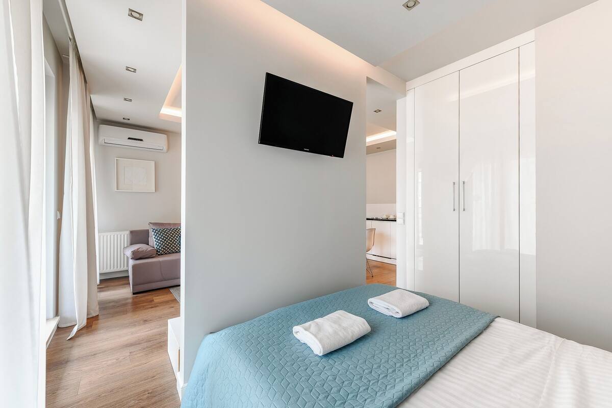 A modern hotel room with a bed, a TV mounted on the wall, and a wardrobe.