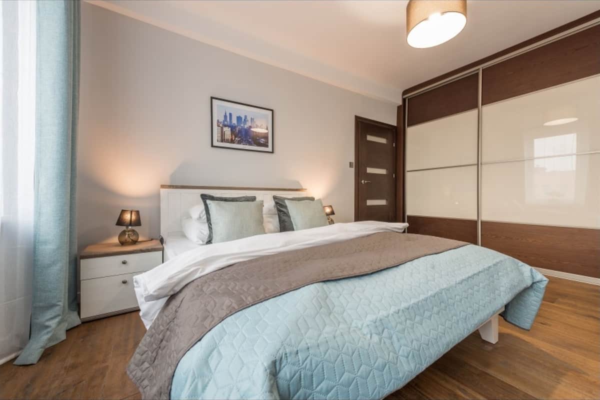 A bedroom with a bed, nightstands, a cityscape picture, a wardrobe, and a door.