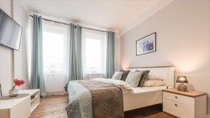 A bedroom with a bed, bedside table, lamp, and a cityscape painting on the wall. - P&O Chimielna 3 (Warsaw)