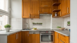 A kitchen with wooden cabinets, a stainless steel oven, a dishwasher, and a window with a plant on the counter. - P&O Chimielna 3 (Warsaw)
