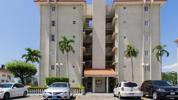 Un hotel de varios pisos con una torre central, balcones y un estacionamiento con coches.
