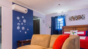 Una habitación con sofá color beige, un cojín rojo, cabecero de madera y pared azul con adornos en espiral.