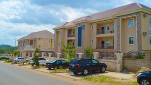 A row of two-story residential buildings with balconies, a parking area with cars, and a clear sky. - Residency Hotel Guzape Abuja (Abuja)