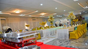 A banquet hall with a long table covered in a white tablecloth, surrounded by yellow chairs, and a buffet setup with silver serving trays. - Residency Hotel Guzape Abuja (Abuja)
