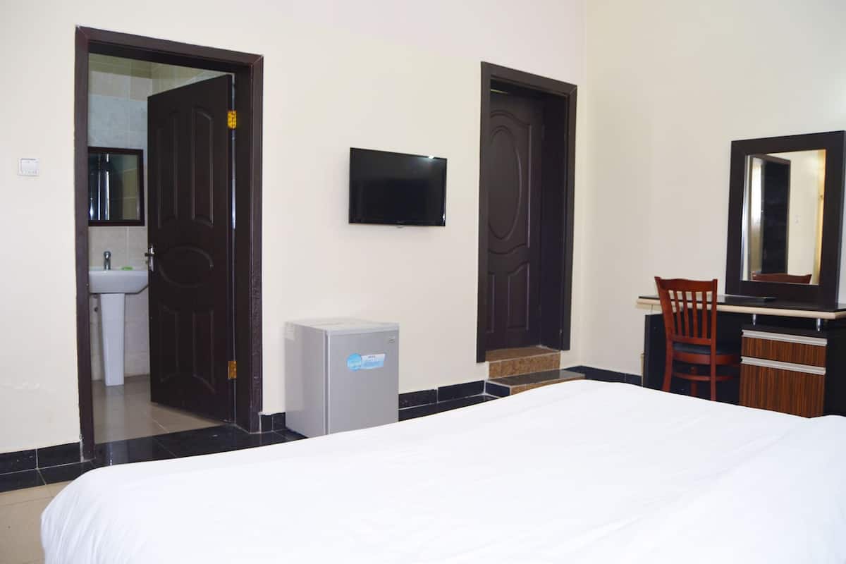 Een hotelkamer met een bed, een bureau met stoel, een aan de muur bevestigde televisie, een kleine koelkast en een deur naar een badkamer.